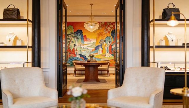 Luxury boutique lounge featuring central round wooden table, colorful mural and crystal chandelier