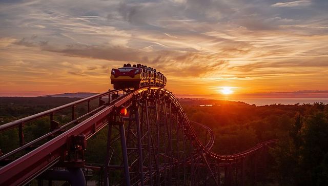 Roller coaster dramatically ascends against breathtaking sunset