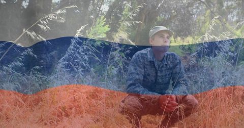 Crouching soldier clasping hands in dry meadow with flag overlay for patriotic themes