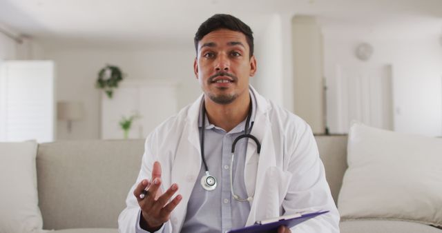 Doctor sitting in a bright and clean clinic discussing a medical diagnosis with a patient. Seen holding a pen and clipboard, wearing a stethoscope and white coat. Ideal for illustrating medical consultations, healthcare discussions, patient interactions, professional medical advice, and the role of healthcare providers.