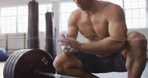 Shirtless athlete preparing for lifting with chalked hands in gym