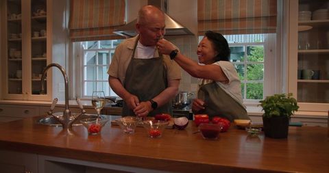 Senior Asian Couple Playfully Cooking Together in Modern Kitchen