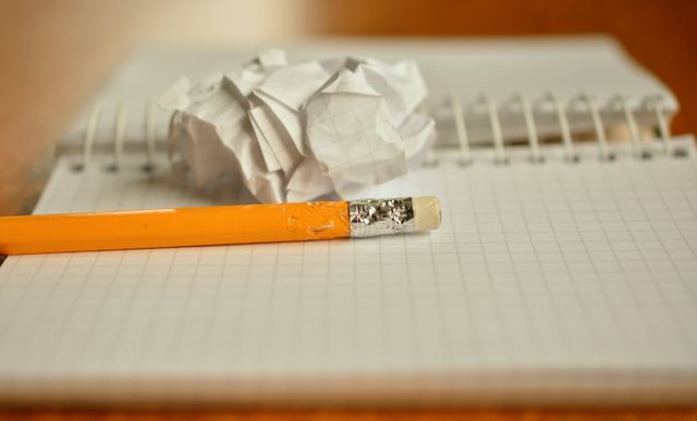 Crumpled paper and a pencil lie on an open grid notebook. Useful for illustrating concepts of writing, planning, making mistakes, corrections, or office supplies.