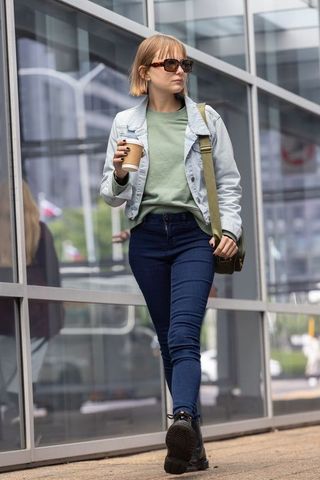 Young woman walking downtown holding coffee cup wearing denim jacket and sunglasses