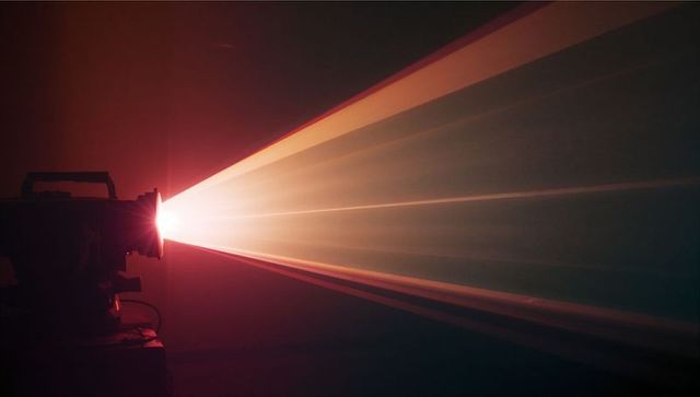 Vintage Film Projector Casting Warm Light Beam in Dark Cinema Room