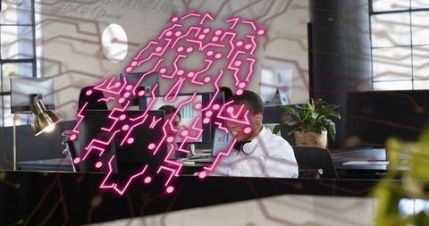 Man working at coworking desk wearing headset focusing on monitors neon circuit overlay