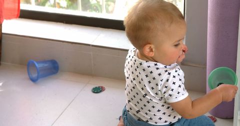 Curious toddler engaged with plastic cups in kitchen