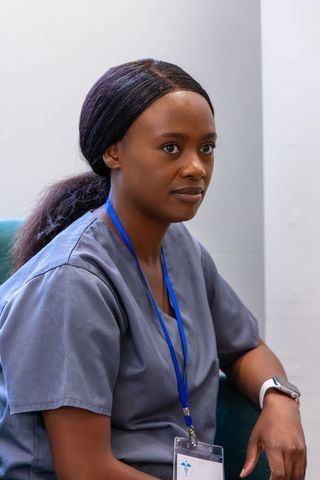 African american nurse sitting in scrubs wearing lanyard and smartwatch in clinic