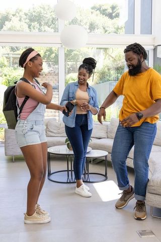 African family dancing, sharing smartphone and sipping coffee in bright modern living room