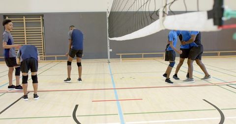 Diverse teenage boys playing volleyball in school gym, preparing for match and teamwork