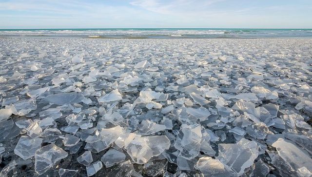 Crystal ice shards covering black sand beach, glinting waves on horizon
