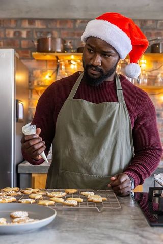 African american baker decorating christmas cookies wearing santa hat and apron