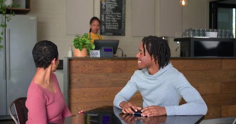 Diverse friends chatting and laughing at cafe table with smartphone and barista nearby