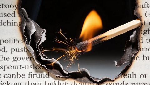 Wooden match igniting with bright sparks through burned paper hole, macro closeup