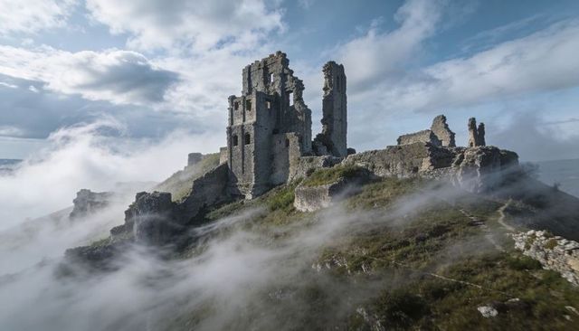 Fog-shrouded coastal castle ruins towering on rocky promontory with winding path