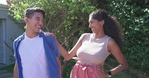 Smiling african american couple sharing laugh in sunlit backyard, woman wearing smartwatch