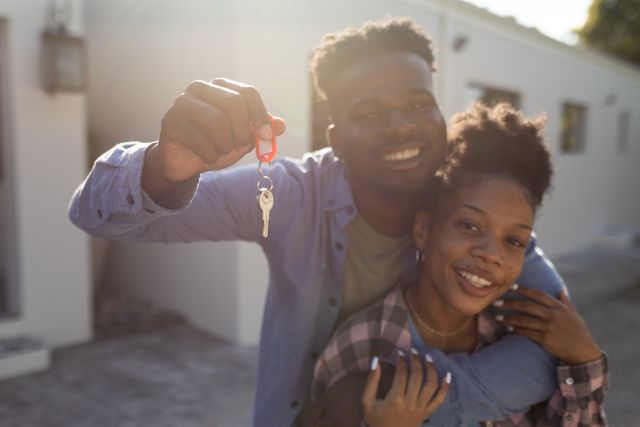 Young african american couple celebrating new home purchase, holding key and smiling. Ideal for real estate promotions, homeownership campaigns, and lifestyle blogs.
