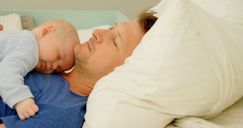 Father Relaxing with Sleeping Baby on Chest in Bedroom