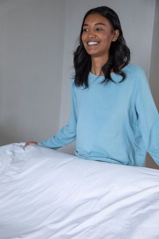 Smiling Woman Making Bed with White Duvet in Minimalist Bedroom