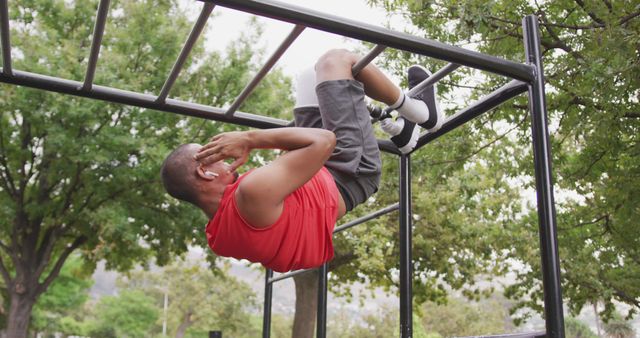 Man executing hanging leg raises on monkey bars in an outdoor park. Perfect for promoting fitness, outdoor exercise, healthy lifestyle, and athletic activities. Can be used for health and fitness websites, workout apps, fitness blogs, and brochures on physical training.