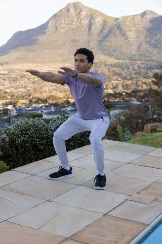 Man Performing Squat on Patio with Mountain Backdrop