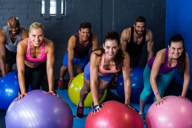 Portrait of athletes smiling while exercising on fitness ball in gym