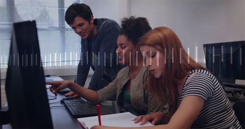 Students collaborating at computer lab, pointing at monitor and taking notes during study