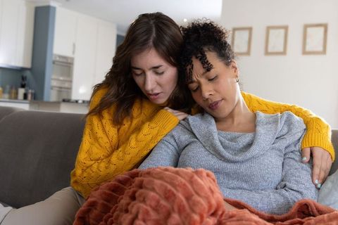 Multiracial couple cuddling on sofa sharing blanket cozy intimate home comfort