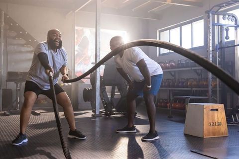 African american men powering through battle-rope workout in sunlit industrial gym