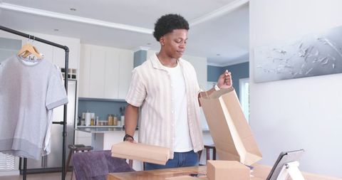 Young entrepreneur packing apparel orders at kitchen table for home based ecommerce business