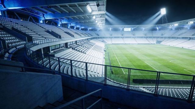 Nighttime modern floodlit football stadium with empty seating tiers and pristine pitch