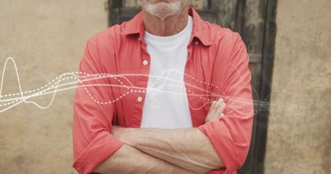 Confident senior man standing with arms crossed wearing red shirt and white tee, weathered wall