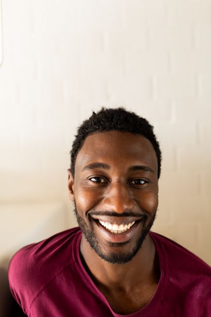 Vertical portrait of happy african american man looking to camera smiling at home, copy space. Domestic life, living alone, relaxation, inclusivity and lifestyle.