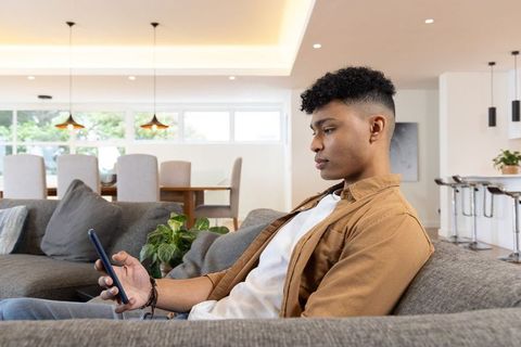African american man relaxing on gray sofa using smartphone in modern open-plan home
