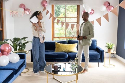 At-home birthday celebration couple wearing sash with cake, balloons, navy velvet sofa