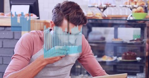 Freelancer working on tablet while sipping coffee in cozy bakery with blue data overlay