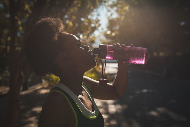 African american female exercising outdoors drinking water in sunny street. healthy outdoor lifestyle fitness training.
