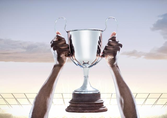 Hands holding a champions trophy high against a stadium background. This image can be used to represent victory, success, and achievement in sports or competitions. Ideal for motivational posters, sports event promotions, and articles on winning and accomplishments.