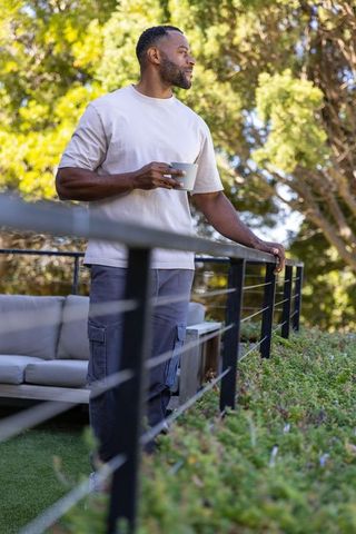 African american man enjoying morning coffee on sunny deck, relaxing outdoor lifestyle