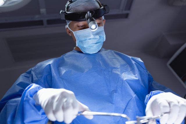 This stock photo captures a focused surgeon performing a delicate operation in a hospital's operating room. The low angle view emphasizes the seriousness and skill involved in the surgical procedure. Ideal for use in healthcare articles, medical blogs, educational resources, and hospital promotional materials.