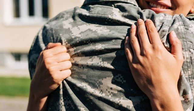 Homecoming embrace between soldier and partner closeup gripping camouflage uniform