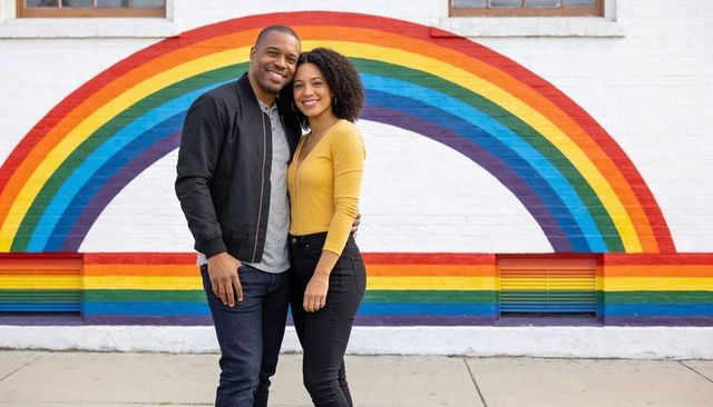 Smiling couple embracing in front of vibrant rainbow mural on urban sidewalk portrait