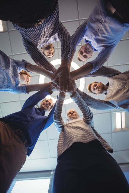 Directly below shot of business colleagues stacking hands against ceiling at office