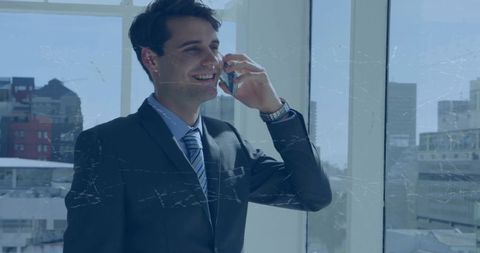 Businessman smiling while talking on phone by office window showing wristwatch and skyline