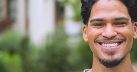 Smiling man with nose stud outdoors shows joyful expression