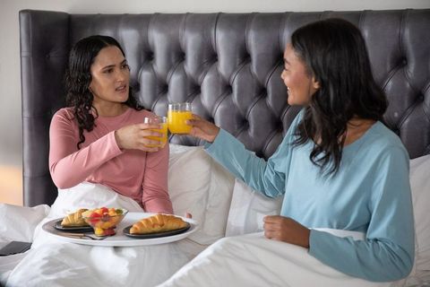 Female Friends Enjoying Breakfast in Bed with Croissants and Orange Juice