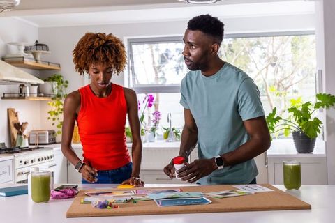 African american couple working on home craft project at bright kitchen island with glue