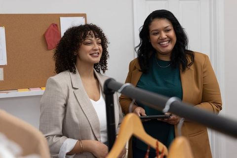 Diverse women collaborating in boutique showroom reviewing garments on rack