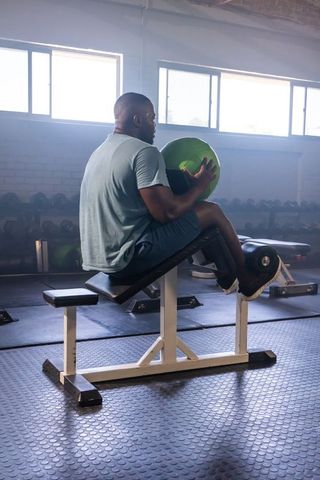 African american man holding green medicine ball on incline ab bench working core