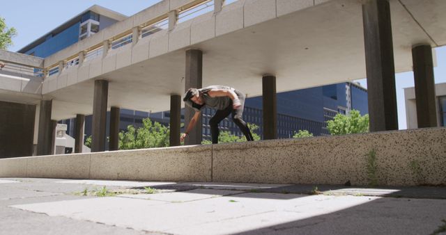 Man performing parkour movement on concrete structure in city setting. Ideal for content related to fitness, extreme sports, urban activities, and athletic training. Perfect for websites, blogs, social media posts, and marketing materials promoting physical activity and agility sports.
